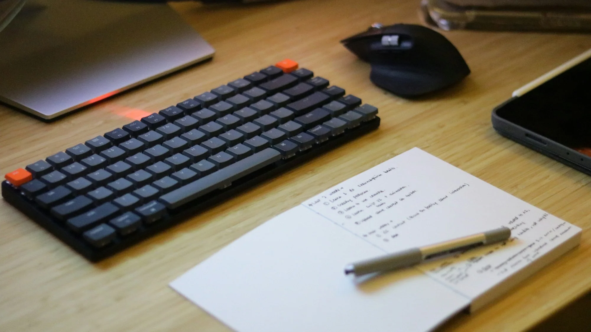 A desk with keyboard, mouse, cell phone and notepad